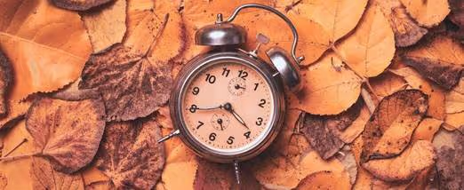 Analog alarm clock against a fall leaves background: daylight savings time