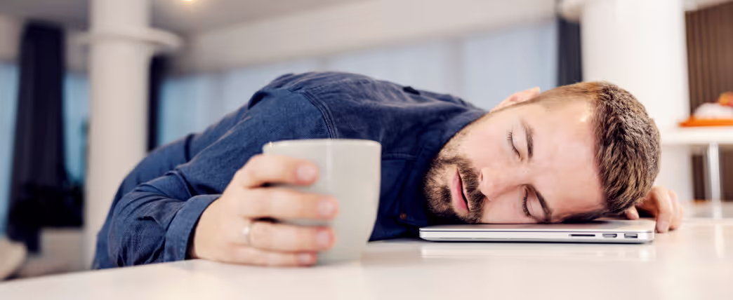 Hombre cansado dormido en el escritorio con una taza de café, intentando quitarse el sueño