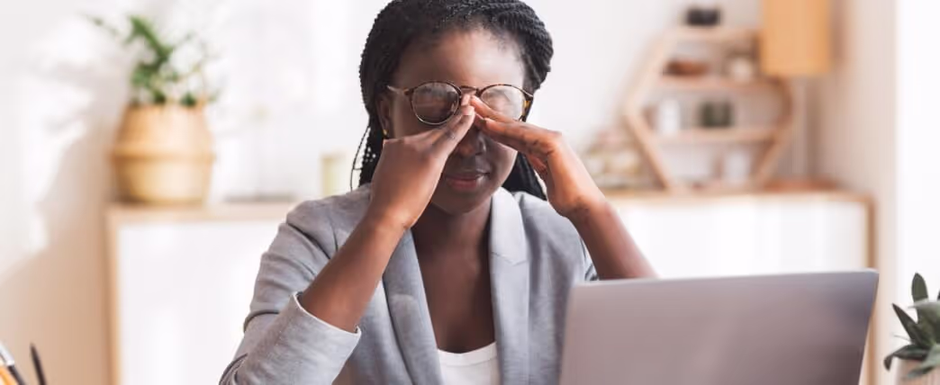 Mujer sentada frente a una laptop frotándose los ojos por no dormir lo suficiente