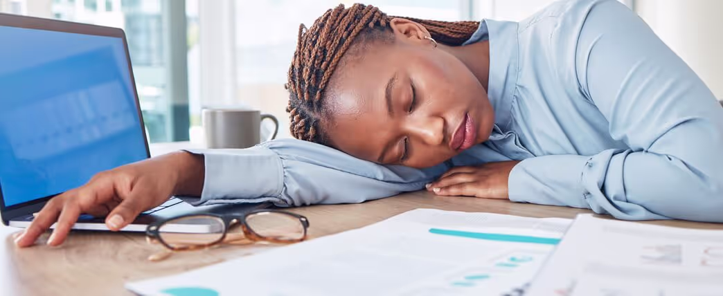 Mulher dormindo na mesa de trabalho por causa do cansaço mental